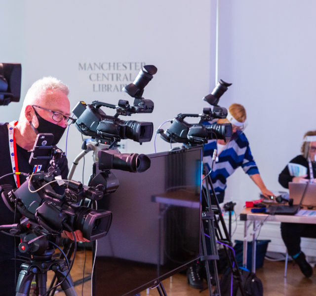 Image of camera operator and film kit in action with two palantypists working in the background in the DigiFest pop up studio in Performance Space, Manchester Central Library.