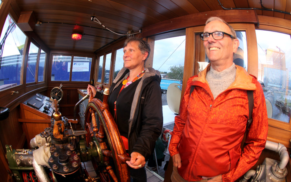 Two people in the front cabin of the Danny steam ship one is holding onto the ships wheel