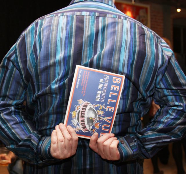 Back of man in striped shirt holding a Belle Vue Programme