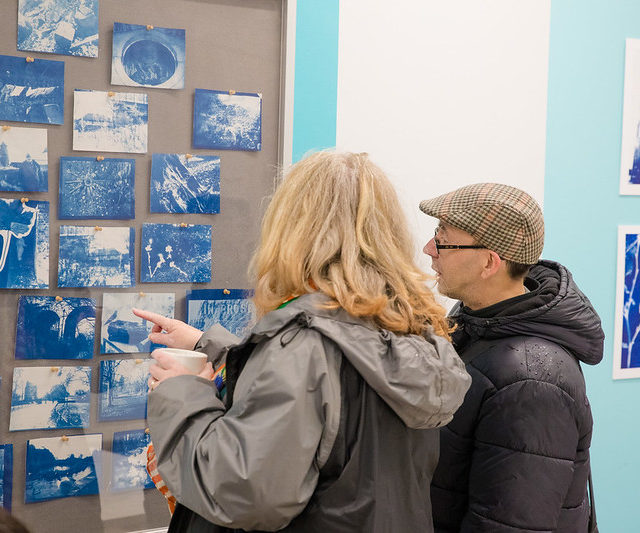 Back of heads of man and woman looking at a set of photography on a pin board