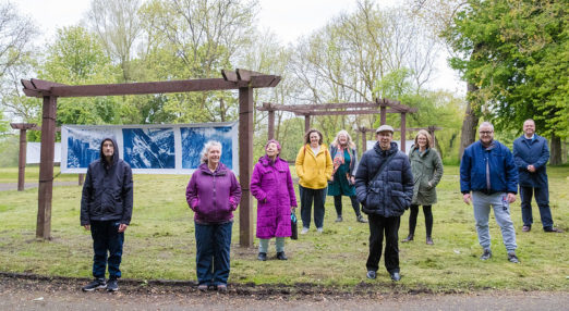 Group of people stood in a park in front of wooden structure exhibiting a photography exhibition