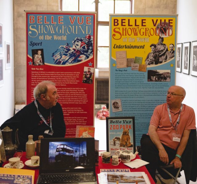 Belle Vue Banners - two men sitting behind table with Belle Vue memorabilia