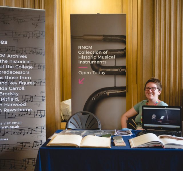 RNCM stand at Manchester Histories Festival Woman sat behind table with a computer and some books on