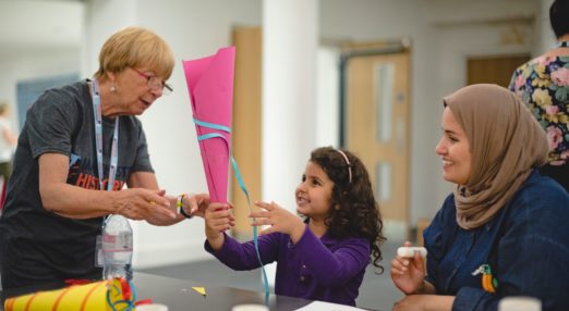 Young girl making paper horn with a Manchester Histories volunteer