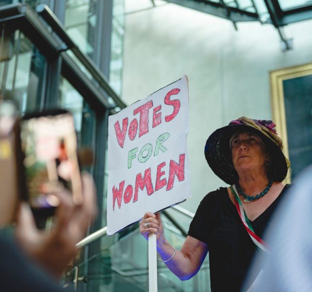 Woman holding banners saying votes for women