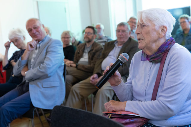 woman speaking into a microphone with audiences in the back
