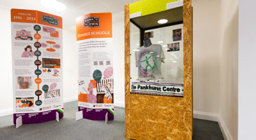 Close up of exhibition panels including a cabinet with a Pankhurst Centre t-shirt and scarf