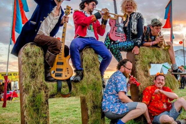 Image of Galivantes - musicians sitting on a hay stack smiling funky and happy