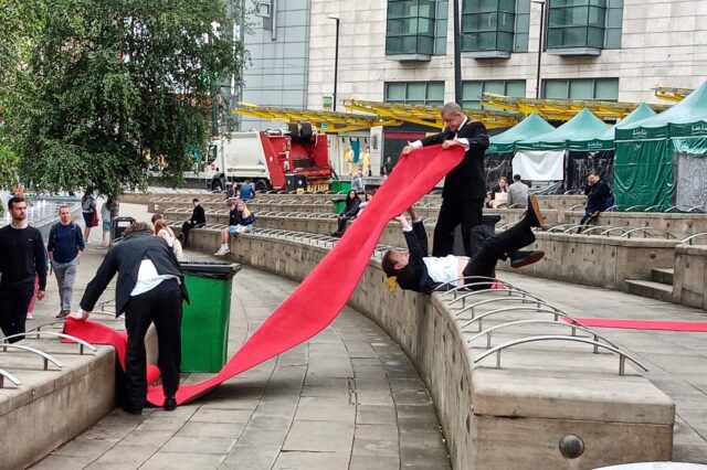 Three men holding up a red carpet in a comic way