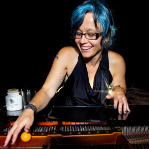 Caro C playing a keyboard a woman with blue hair glasses and wearing black