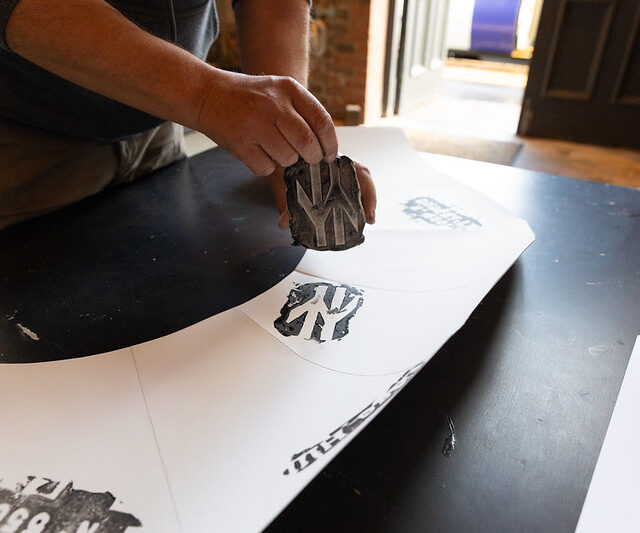 A person's hand printing a british rail sign on a blank piece of paper shaped in an arch