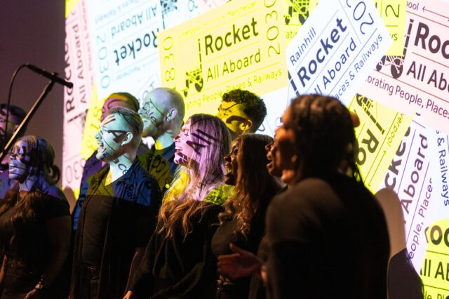 Choir singing a song - a group of young people against a backdrop of the Rocket: All Aboard logo