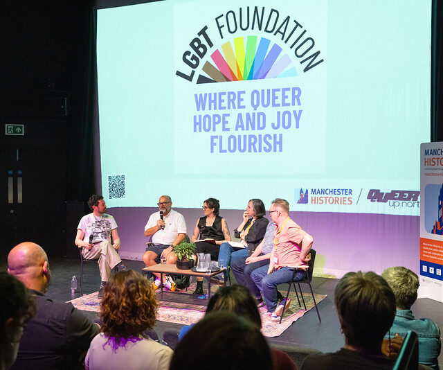 An image of a panel of people sat on chairs at at QUN North Event LGBT Foundation screen can be seen behind the speakers it says Where Queer Hope & Joy Flourish