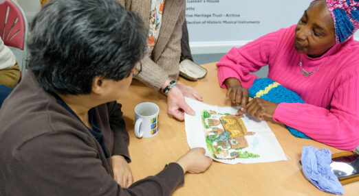 People looking at a textile of a embroidered cottage