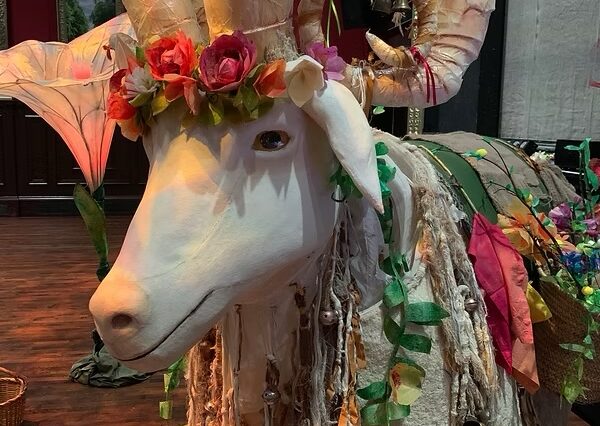 An image of a goat with horns dresses in colourful flowers
