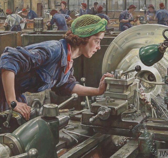 A woman leaning over a machine - she is dressed in WW2 overalls and has a green headscarf wrapped around her hair